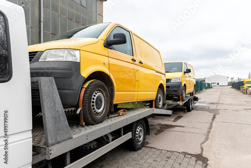Fotografi White small cargo truck car carrier loaded with two yellow van minibus on flatbed platform and semi trailer tow on roadside highway road