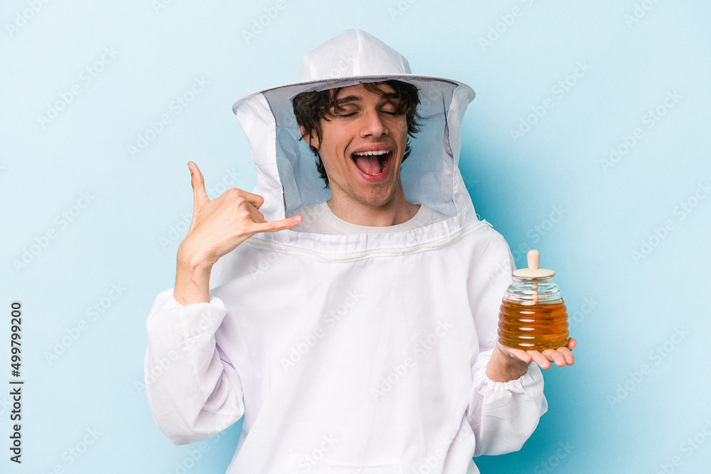 Young caucasian beekeeper man isolated on blue background showing a mobile phone call gesture with fingers. Young caucasian beekeeper man isolated on blue background showing a mobile phone call gesture with fingers.