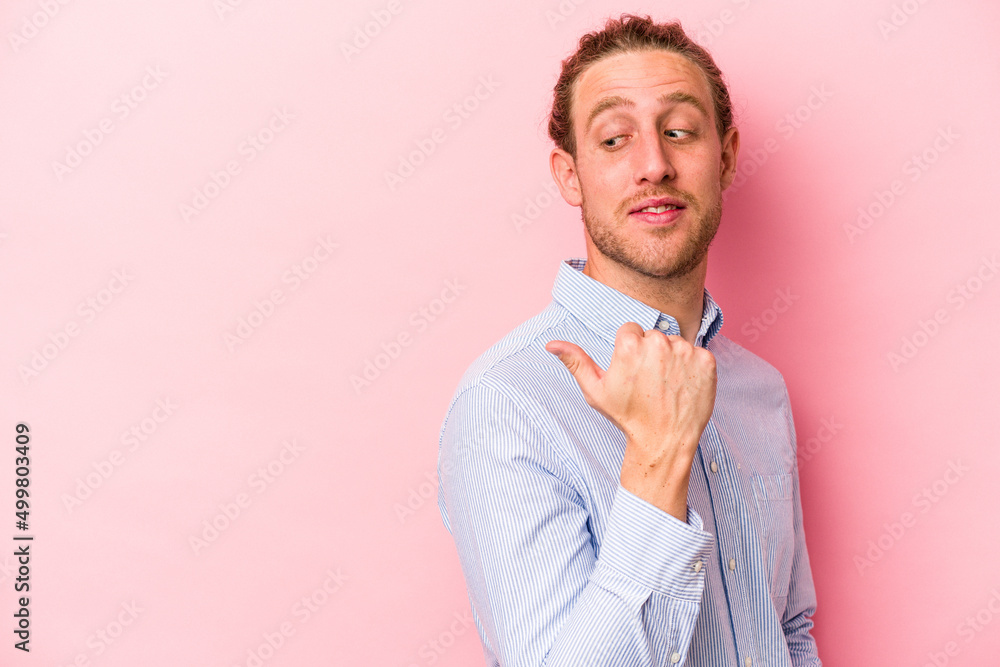 Young caucasian man isolated on pink background points with thumb finger away, laughing and carefree. Young caucasian man isolated on pink background points with thumb finger away, laughing and carefree.