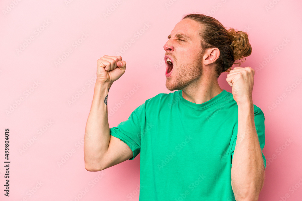 Young caucasian man isolated on pink background raising fist after a victory, winner concept. Young caucasian man isolated on pink background raising fist after a victory, winner concept.