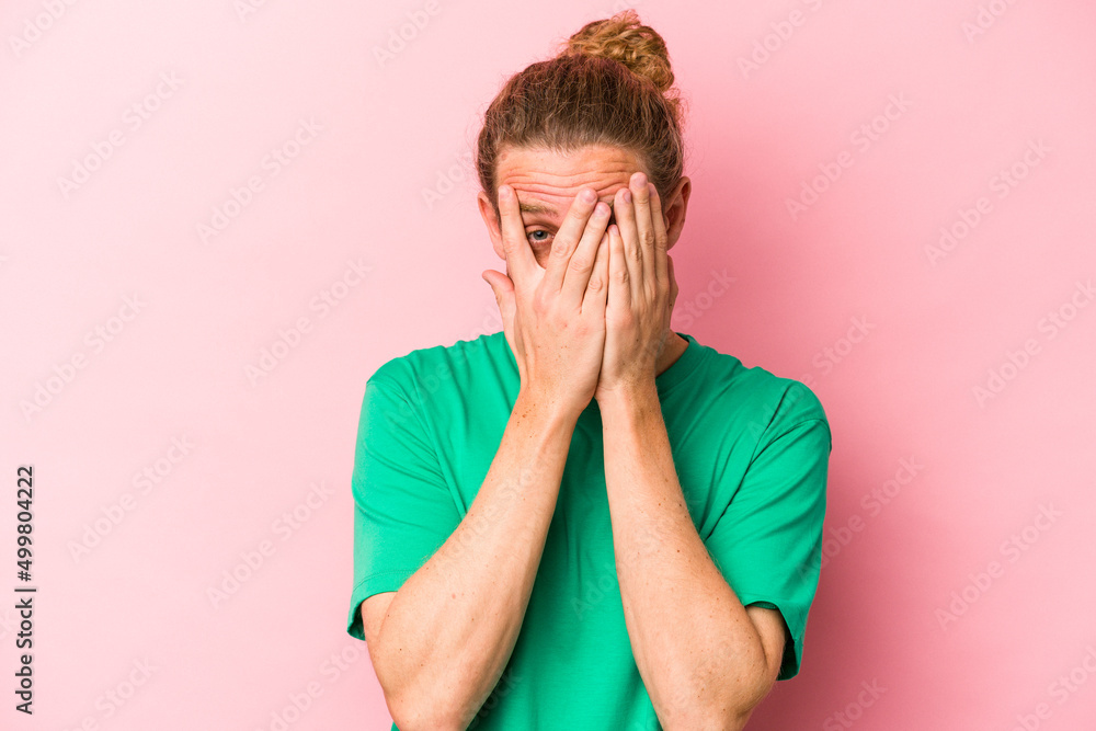 Young caucasian man isolated on pink background blink through fingers frightened and nervous. Young caucasian man isolated on pink background blink through fingers frightened and nervous.