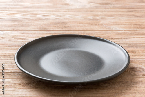 Perspective view of empty black plate on wooden background. Empty space for your design