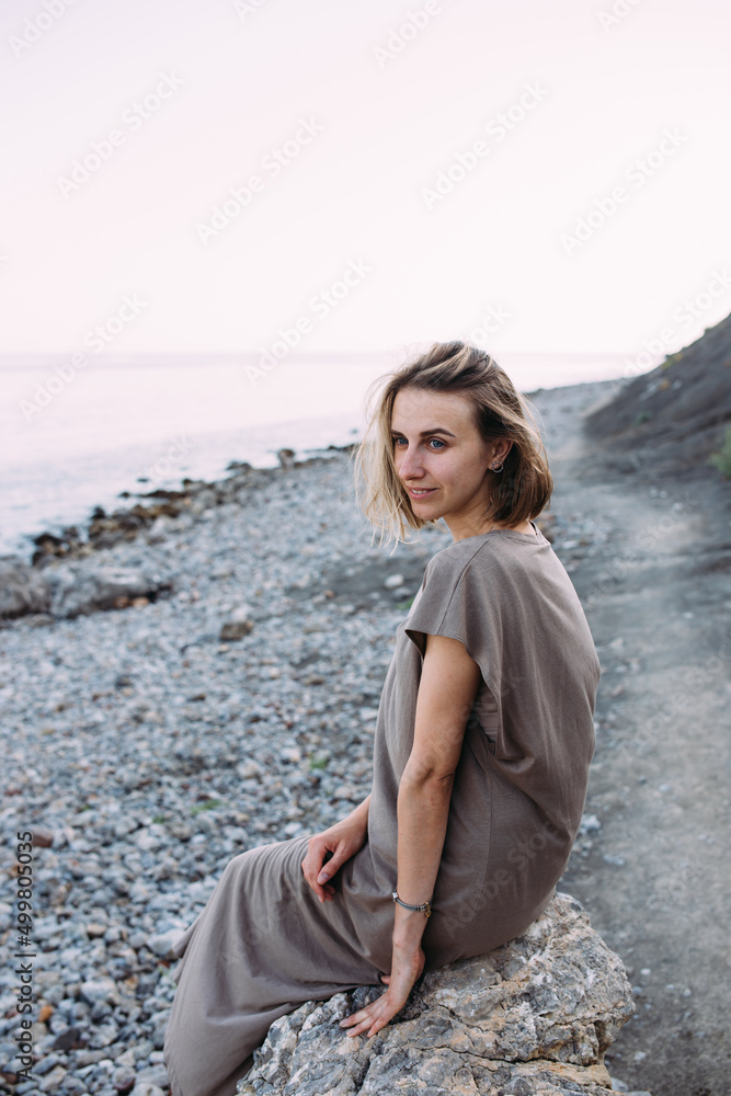 Beautiful relaxed young woman sits on a stone near the sea. Beautiful relaxed young woman sits on a stone near the sea.