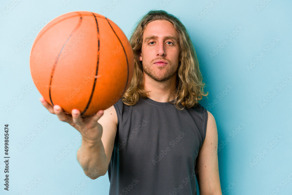 Young caucasian man playing basketball isolated on blue background Young caucasian man playing basketball isolated on blue background