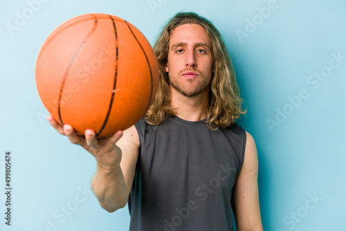 Young caucasian man playing basketball isolated on blue background