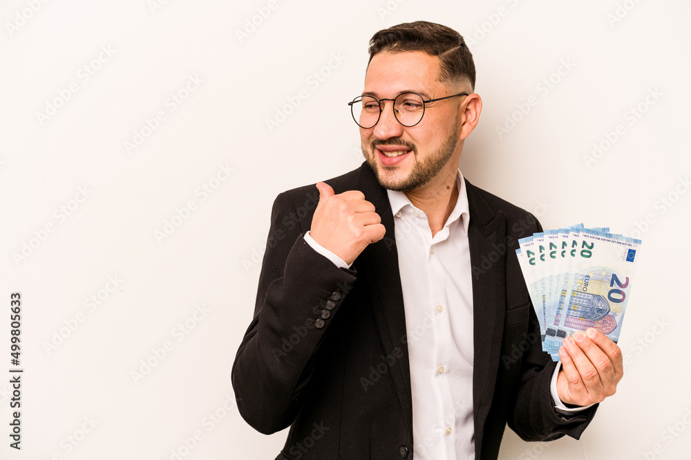 Business hispanic man holding banknotes isolated on white background points with thumb finger away, laughing and carefree. Business hispanic man holding banknotes isolated on white background points with thumb finger away, laughing and carefree.