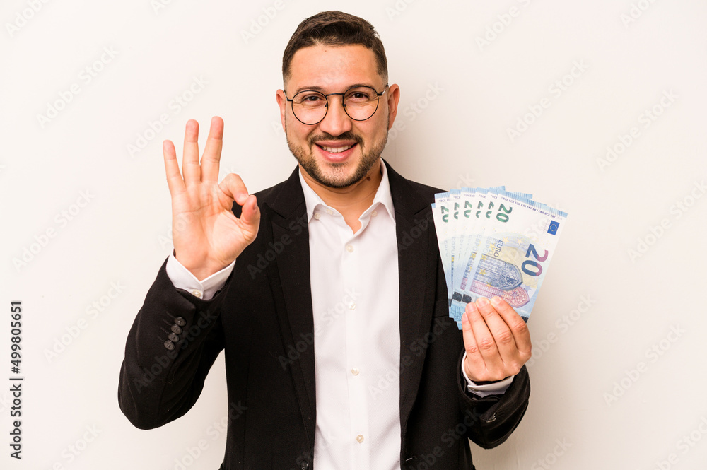 Business hispanic man holding banknotes isolated on white background cheerful and confident showing ok gesture. Business hispanic man holding banknotes isolated on white background cheerful and confident showing ok gesture.