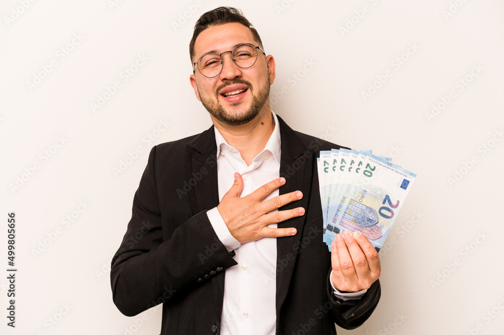 Business hispanic man holding banknotes isolated on white background laughs out loudly keeping hand on chest. Business hispanic man holding banknotes isolated on white background laughs out loudly keeping hand on chest.
