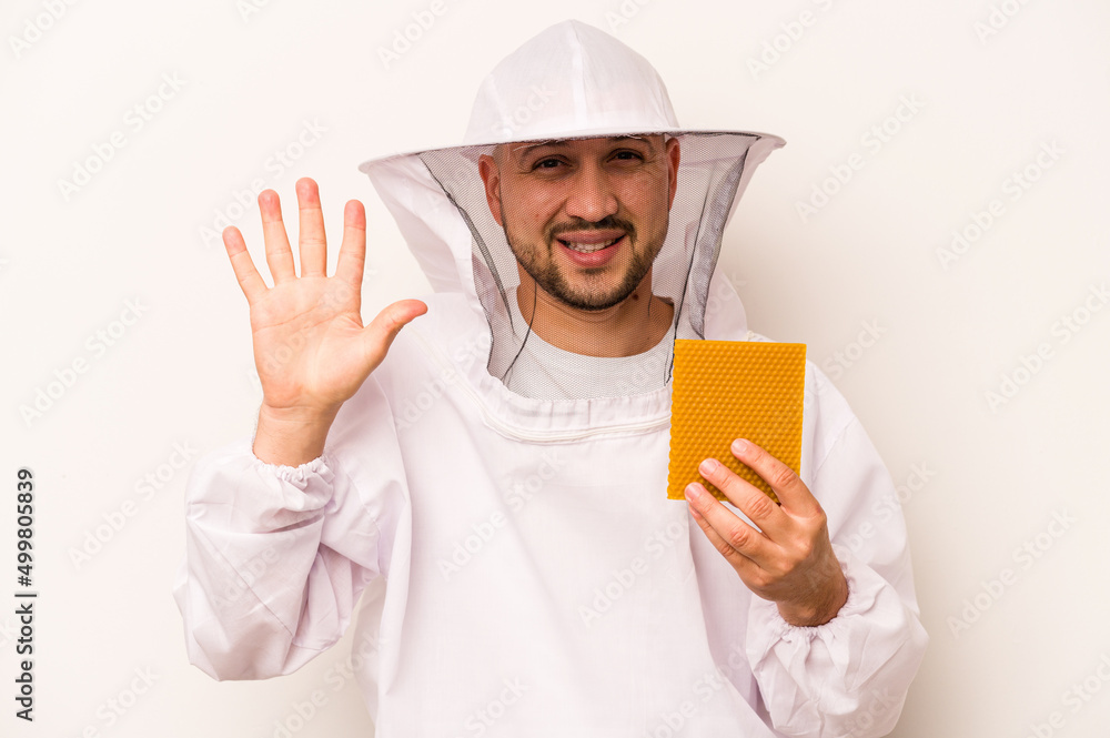 Hispanic beekeeper man holding honey isolated on white background smiling cheerful showing number five with fingers. Hispanic beekeeper man holding honey isolated on white background smiling cheerful showing number five with fingers.