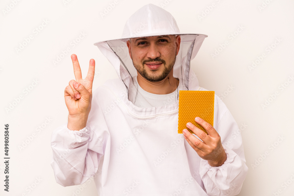 Hispanic beekeeper man holding honey isolated on white background showing number two with fingers. Hispanic beekeeper man holding honey isolated on white background showing number two with fingers.