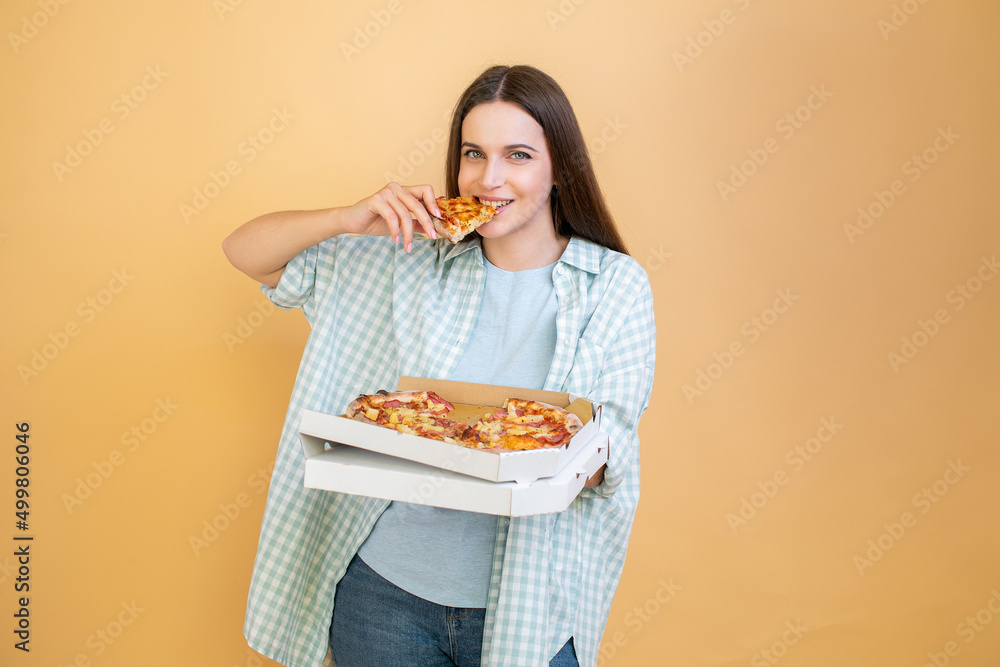 Happy young woman holding hot pizza in box and bites piece of pizza
