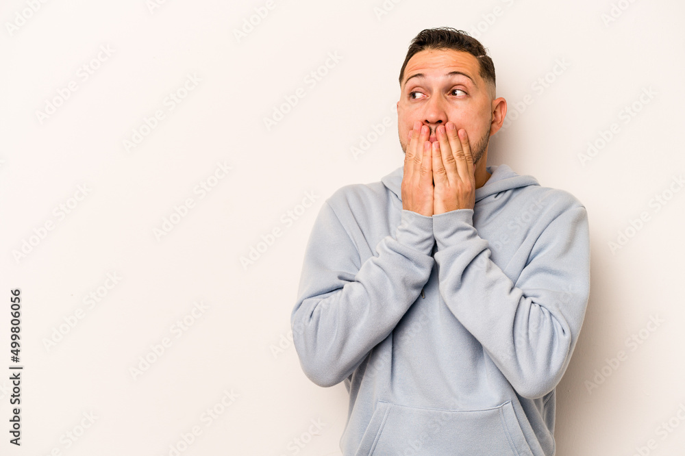 Young hispanic man isolated on white background thoughtful looking to a copy space covering mouth with hand. Young hispanic man isolated on white background thoughtful looking to a copy space covering mouth with hand.