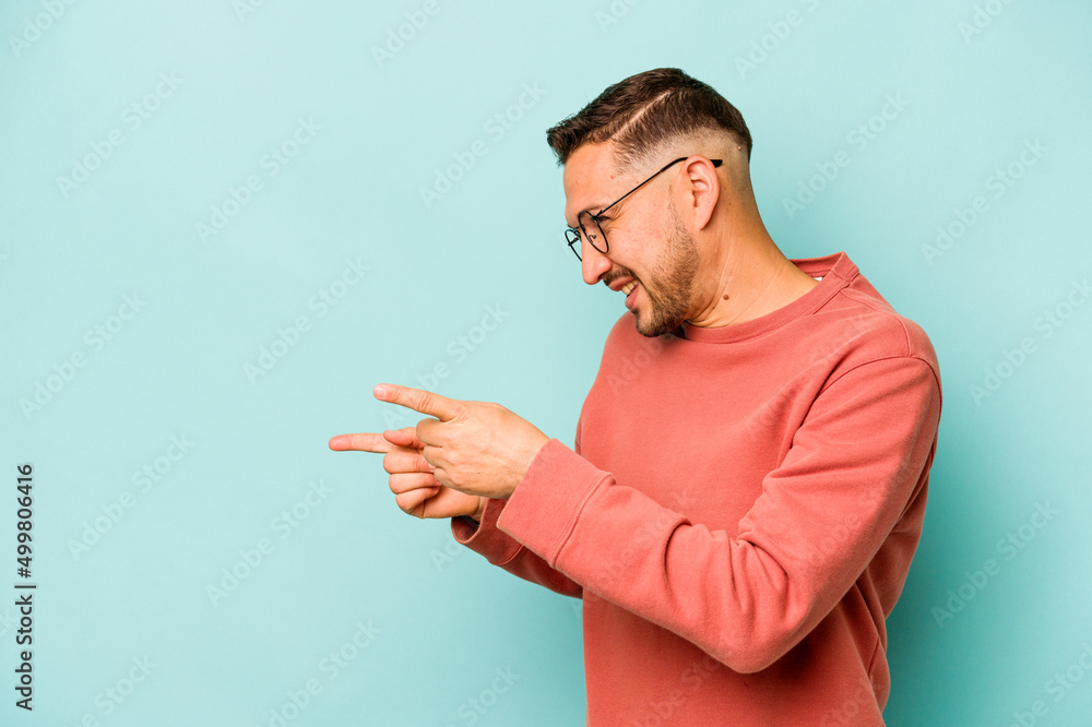 Young hispanic man isolated on blue background points with thumb finger away, laughing and carefree. Young hispanic man isolated on blue background points with thumb finger away, laughing and carefree.
