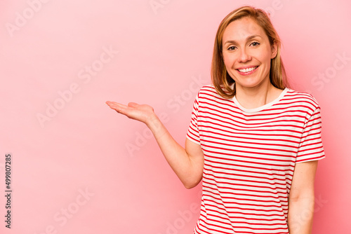 Young caucasian woman isolated on pink background showing a copy space on a palm and holding another hand on waist.