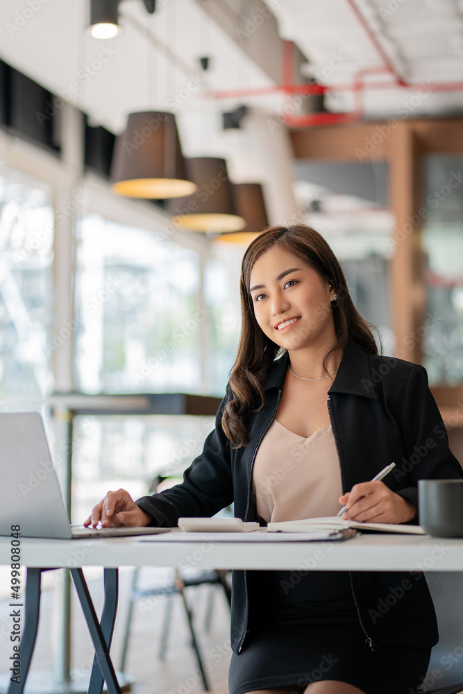 Φωτογραφία Smiling Asian businesswoman working on paper and holding pen and laptop sitting on a chair at modern home studio