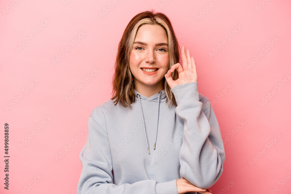 Young caucasian woman isolated on pink background winks an eye and holds an okay gesture with hand. Young caucasian woman isolated on pink background winks an eye and holds an okay gesture with hand.