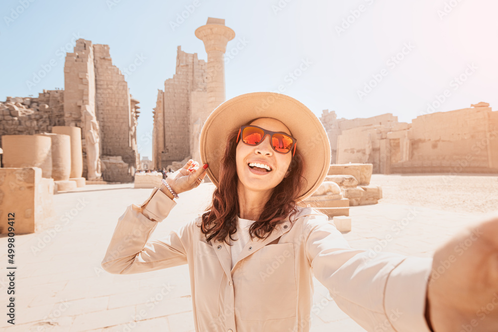 Travel blogger woman takes selfie photos at the ruins of the famous Karnak temple in Luxor or ancient Thebes in Egypt.