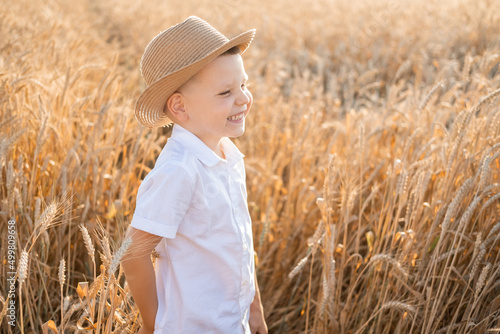 cute smiling child boy in straw hat in wheat field on summer sunset.