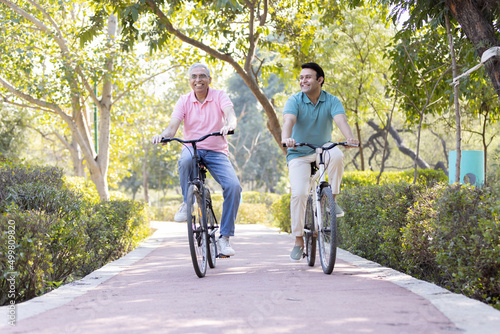 Happy senior man riding bicycle with his young son at park