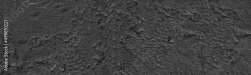 Old weathered black exterior wall wide panoramic texture. Cracked painted plaster. Dark gray grunge widescreen background