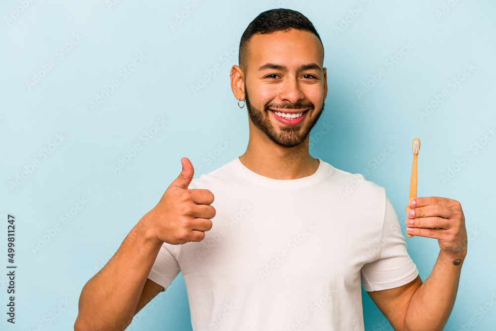 Young hispanic man brushing teeth isolated on blue background smiling and raising thumb up Young hispanic man brushing teeth isolated on blue background smiling and raising thumb up