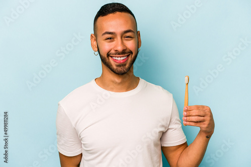 Young hispanic man brushing teeth isolated on blue background laughing and having fun.