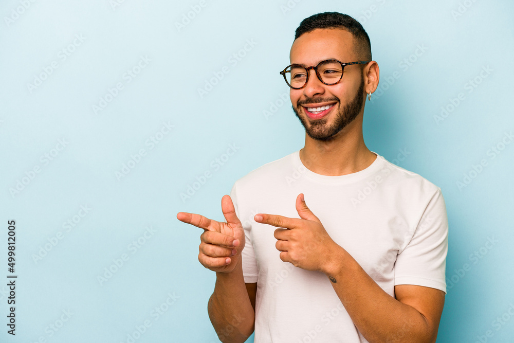 Young hispanic man isolated on blue background points with thumb finger away, laughing and carefree. Young hispanic man isolated on blue background points with thumb finger away, laughing and carefree.