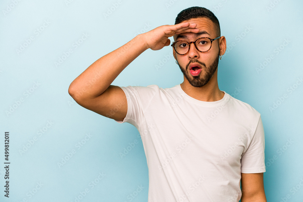 Young hispanic man isolated on blue background looking far away keeping hand on forehead. Young hispanic man isolated on blue background looking far away keeping hand on forehead.