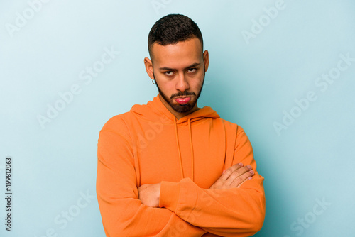 Young hispanic man isolated on blue background tired of a repetitive task.