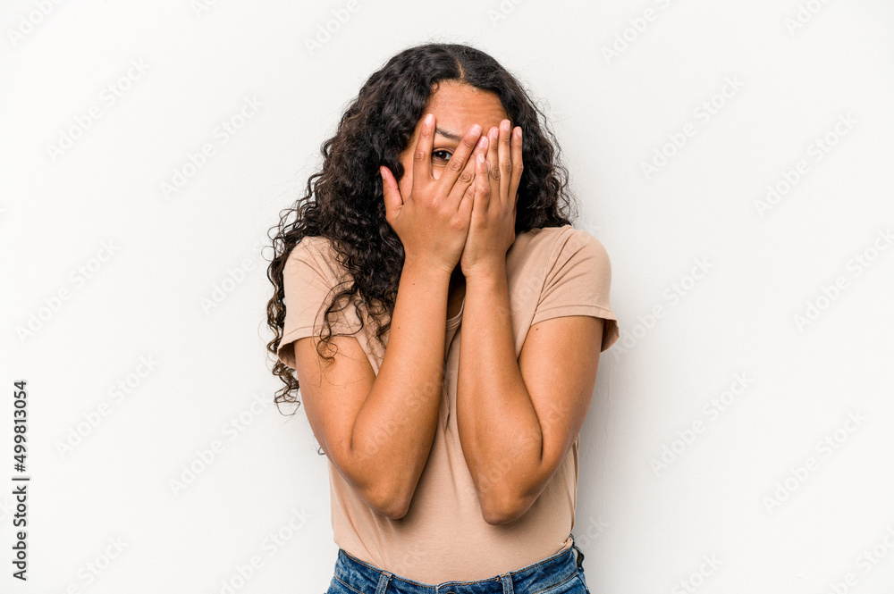 Young hispanic woman isolated on white background blink at the camera through fingers, embarrassed covering face.