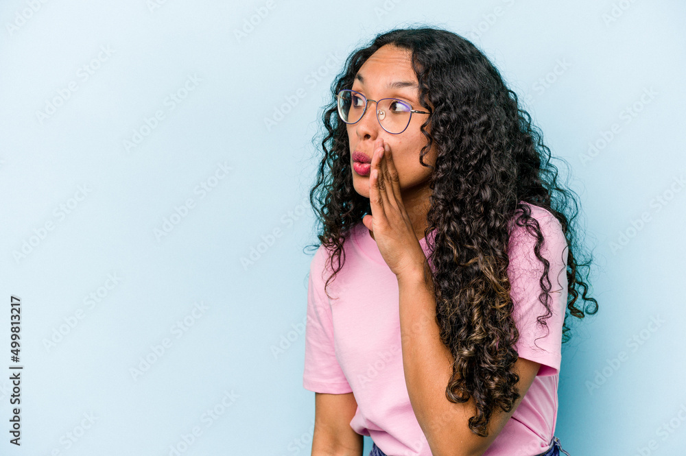Young hispanic woman isolated on blue background is saying a secret hot braking news and looking aside Young hispanic woman isolated on blue background is saying a secret hot braking news and looking aside