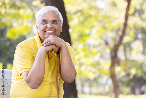 Cheerful senior man sitting on bench with walking stick at park © G-images