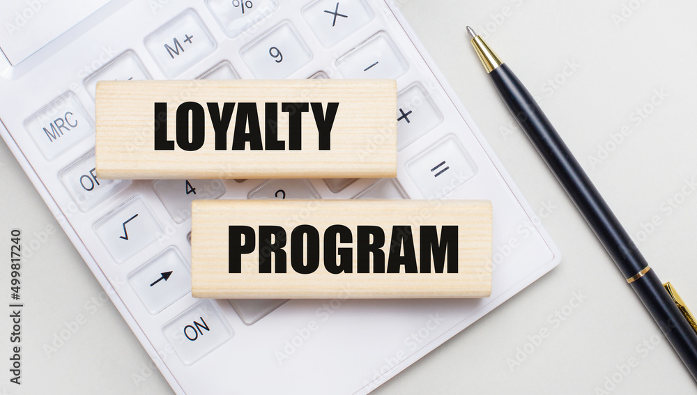 Wooden blocks with the text LOYALTY PROGRAM lie on a light background on a white calculator. Nearby is a black pen. business concept Wooden blocks with the text LOYALTY PROGRAM lie on a light background on a white calculator. Nearby is a black pen. business concept
