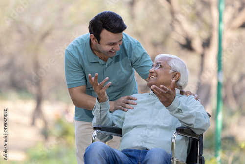 Young man having fun with his father on wheelchair at park
