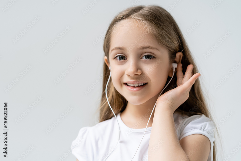 cheerful girl in wired earphones looking at camera isolated on grey. cheerful girl in wired earphones looking at camera isolated on grey.