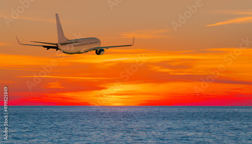 Airplane flying over tropical sea at sunset