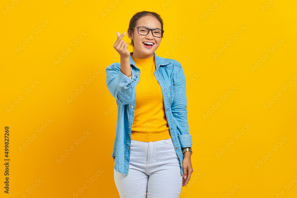 Portrait of smiling young Asian woman student in denim clothes showing korean heart with two fingers crossed isolated on yellow background. People sincere emotions lifestyle concept Portrait of smiling young Asian woman student in denim clothes showing korean heart with two fingers crossed isolated on yellow background. People sincere emotions lifestyle concept