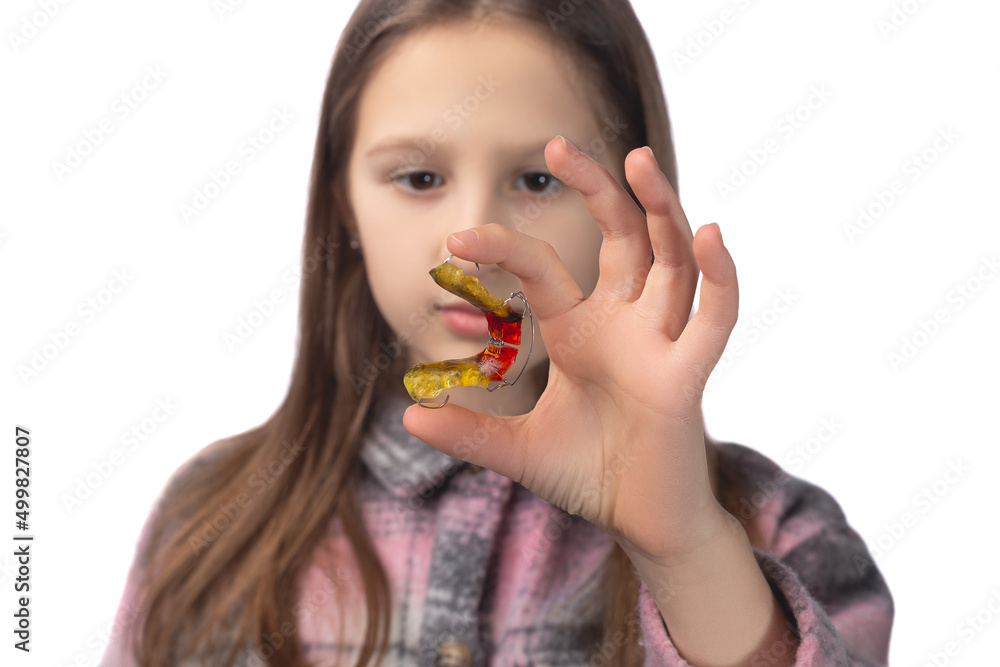Cute little girl posing in the studio holding an orthodontic appliance in her hand. The concept of oral hygiene in childhood. Photo on a white background. Cute little girl posing in the studio holding an orthodontic appliance in her hand. The concept of oral hygiene in childhood. Photo on a white background.