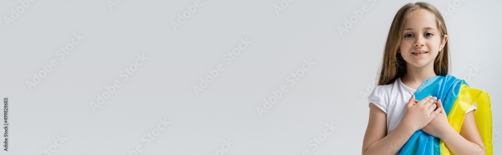 patriotic ukrainian girl with national flag and hands on heart isolated on grey, banner. patriotic ukrainian girl with national flag and hands on heart isolated on grey, banner.
