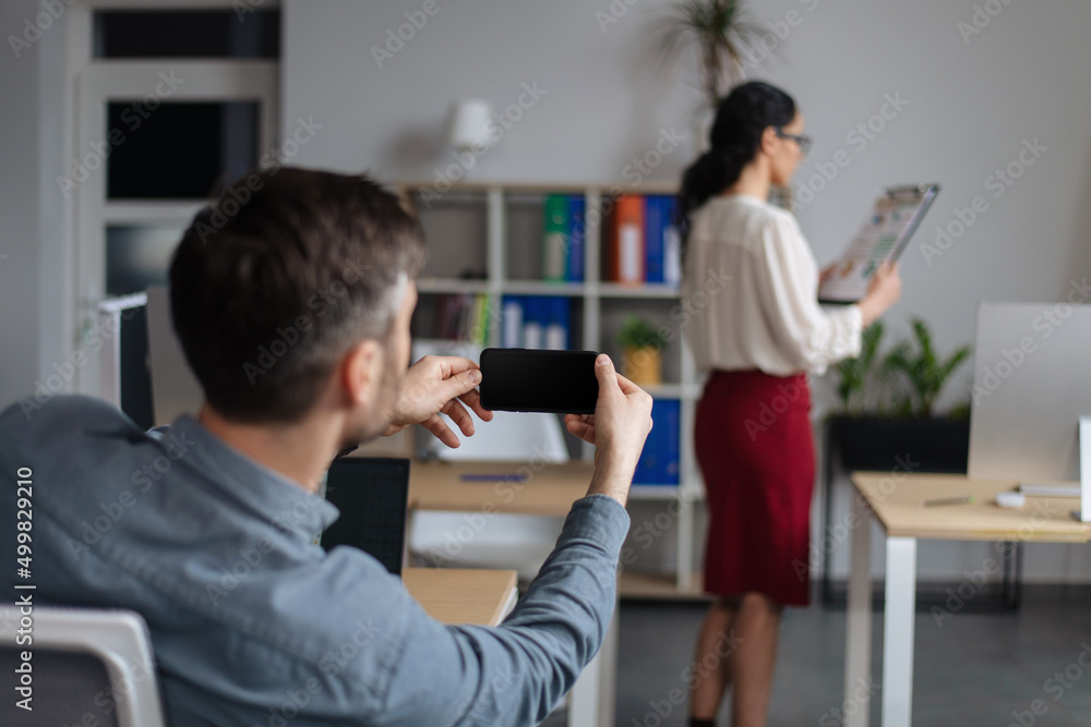 Gender discrimination and career. Perverted guy taking mobile photo of his female colleague without her consent at office Gender discrimination and career. Perverted guy taking mobile photo of his female colleague without her consent at office