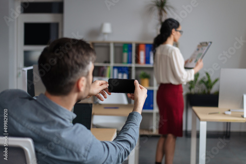 Gender discrimination and career. Perverted guy taking mobile photo of his female colleague without her consent at office photo