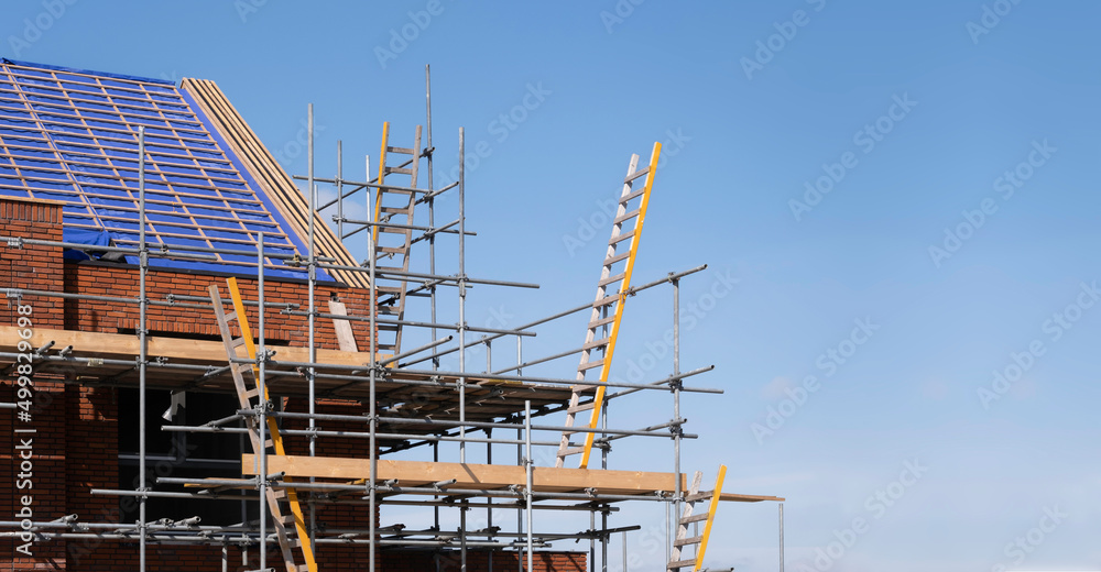 Scaffolding pile platform against a newly built row of houses on a construction site. There are ladders to climb from one platform to another. Wide image, the Netherlands