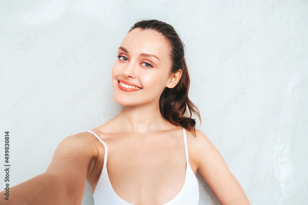 Young beautiful smiling female in trendy summer jeans skirt and top. Sexy carefree woman posing near grey wall in studio. Positive brunette model having fun and going crazy. Taking Pov selfie Young beautiful smiling female in trendy summer jeans skirt and top. Sexy carefree woman posing near grey wall in studio. Positive brunette model having fun and going crazy. Taking Pov selfie