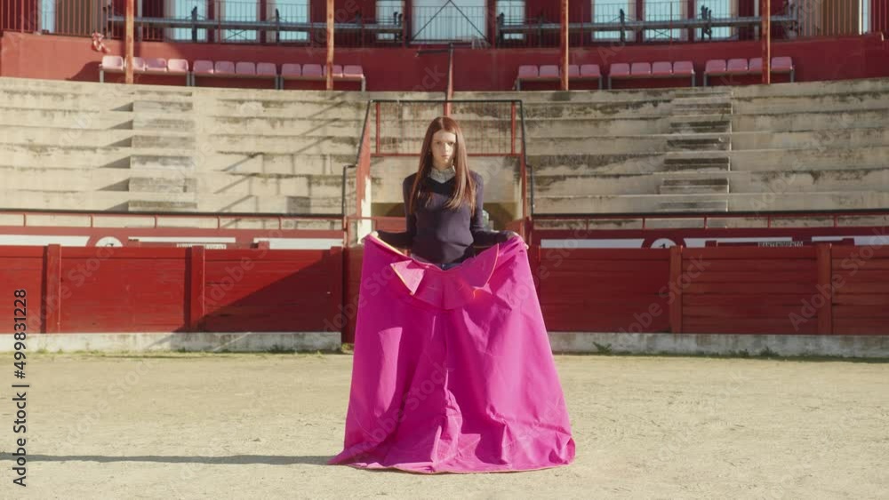 Young Female Bullfighter With Muleta Standing In Middle Of Bullring With Empty Tiered Rows In The Background. - static