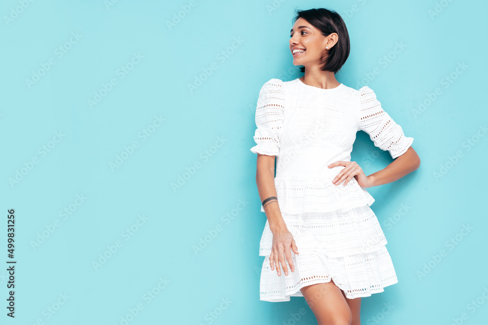 Young beautiful smiling female in trendy summer white dress. Sexy carefree woman posing near blue wall in studio. Positive model having fun. Cheerful and happy. Isolated Young beautiful smiling female in trendy summer white dress. Sexy carefree woman posing near blue wall in studio. Positive model having fun. Cheerful and happy. Isolated