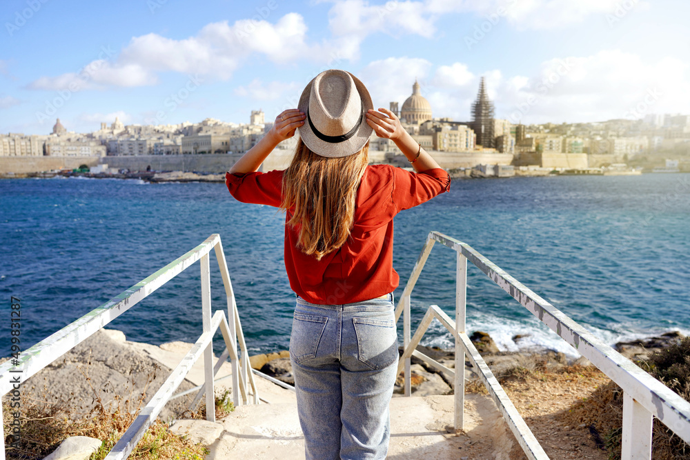 Holidays in Malta. Back view of beautiful girl enjoying view of Valletta cityscape with the blue water of Mediterranean sea.