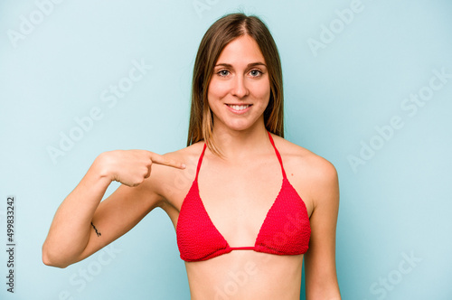 Young caucasian woman going to the beach isolated on blue background person pointing by hand to a shirt copy space, proud and confident © Asier