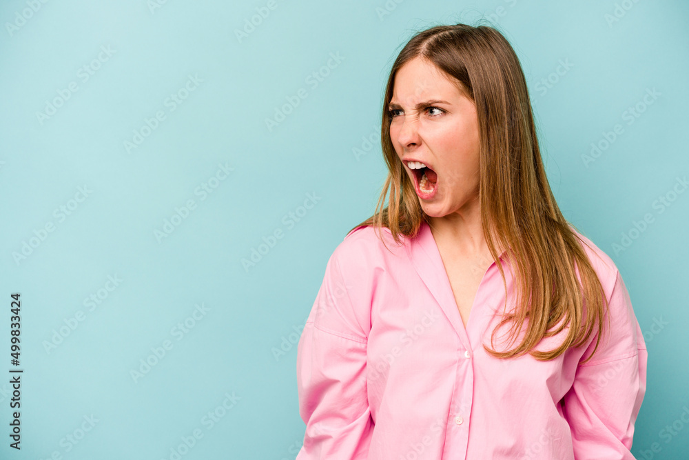 Fototapeta premium Young caucasian woman isolated on blue background shouting very angry, rage concept, frustrated.