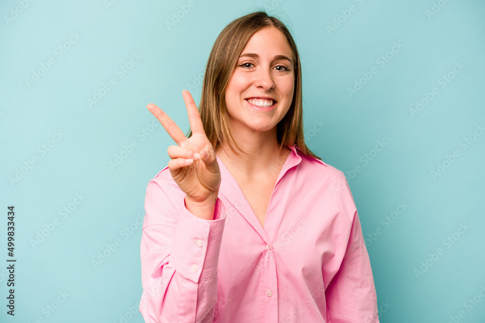 Young caucasian woman isolated on blue background showing victory sign and smiling broadly. Young caucasian woman isolated on blue background showing victory sign and smiling broadly.