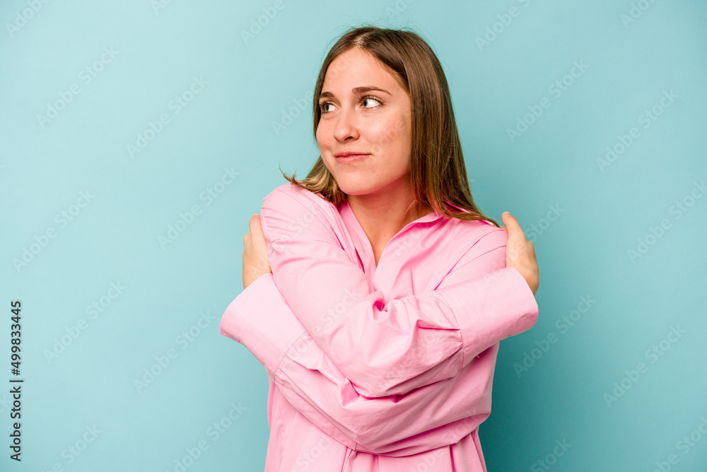 Fototapeta premium Young caucasian woman isolated on blue background hugs, smiling carefree and happy.